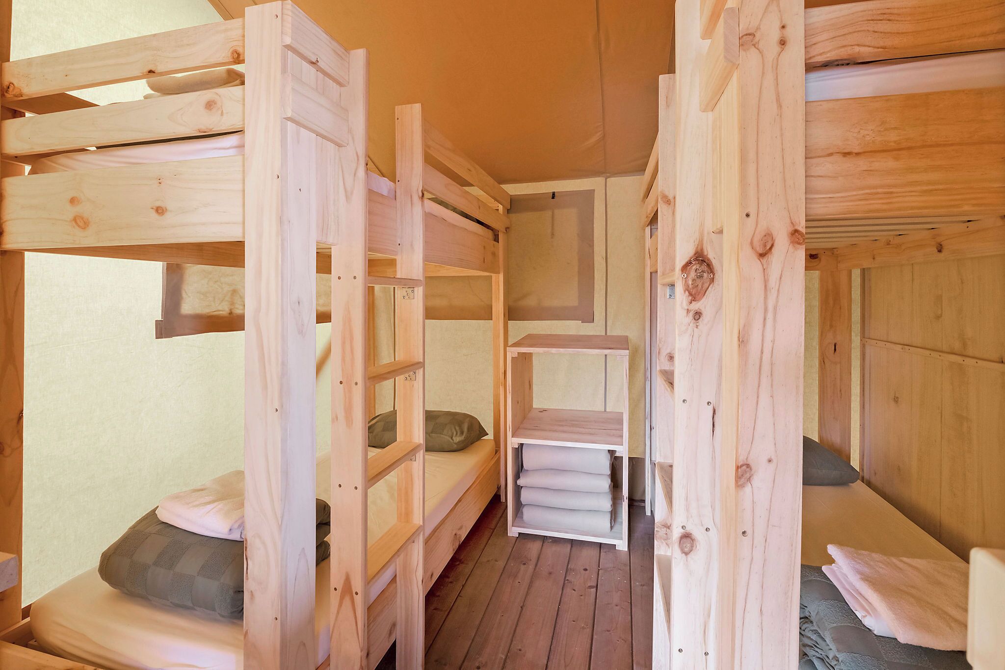 A wooden bunk bed room with a simple layout, including a shelf unit and a small table.