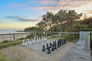 A chessboard set up on a wooden deck with a view of the ocean.