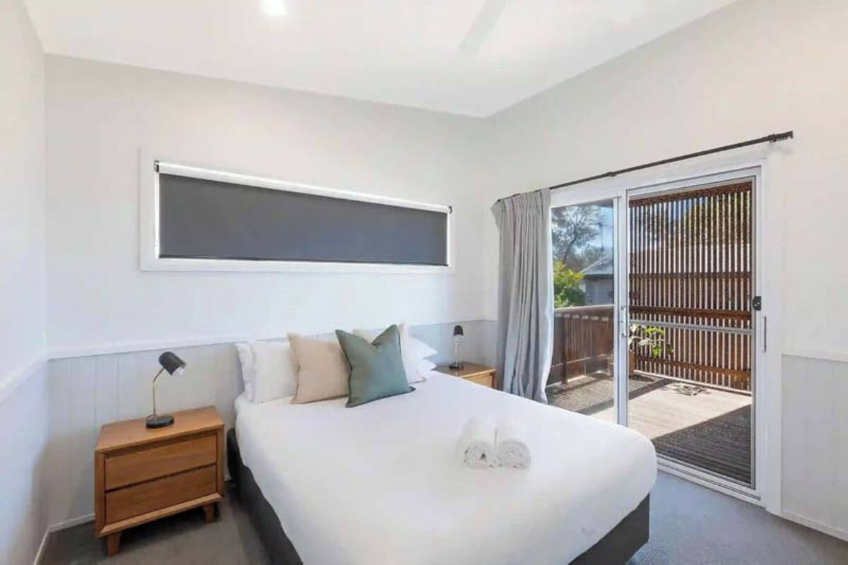 A bedroom with a bed, bedside tables, a window, and a sliding glass door to an outdoor area.
