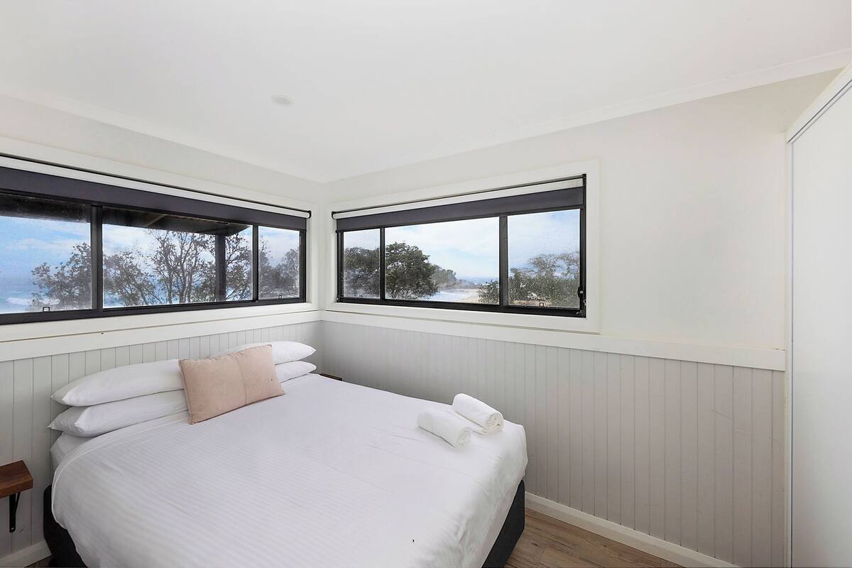 A bedroom with a bed, two windows, and a view of trees.