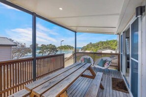 A wooden deck with a table and chairs, overlooking a beach and hills.