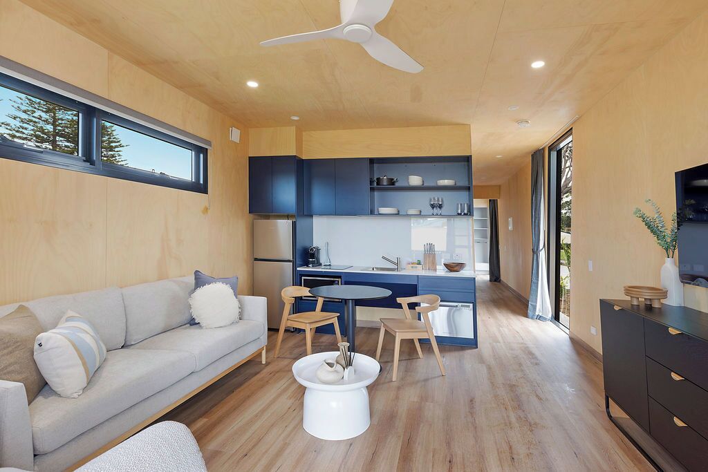 Een modern interieur met een bank, eettafel, stoelen, een keukenhoek en een plafondventilator.