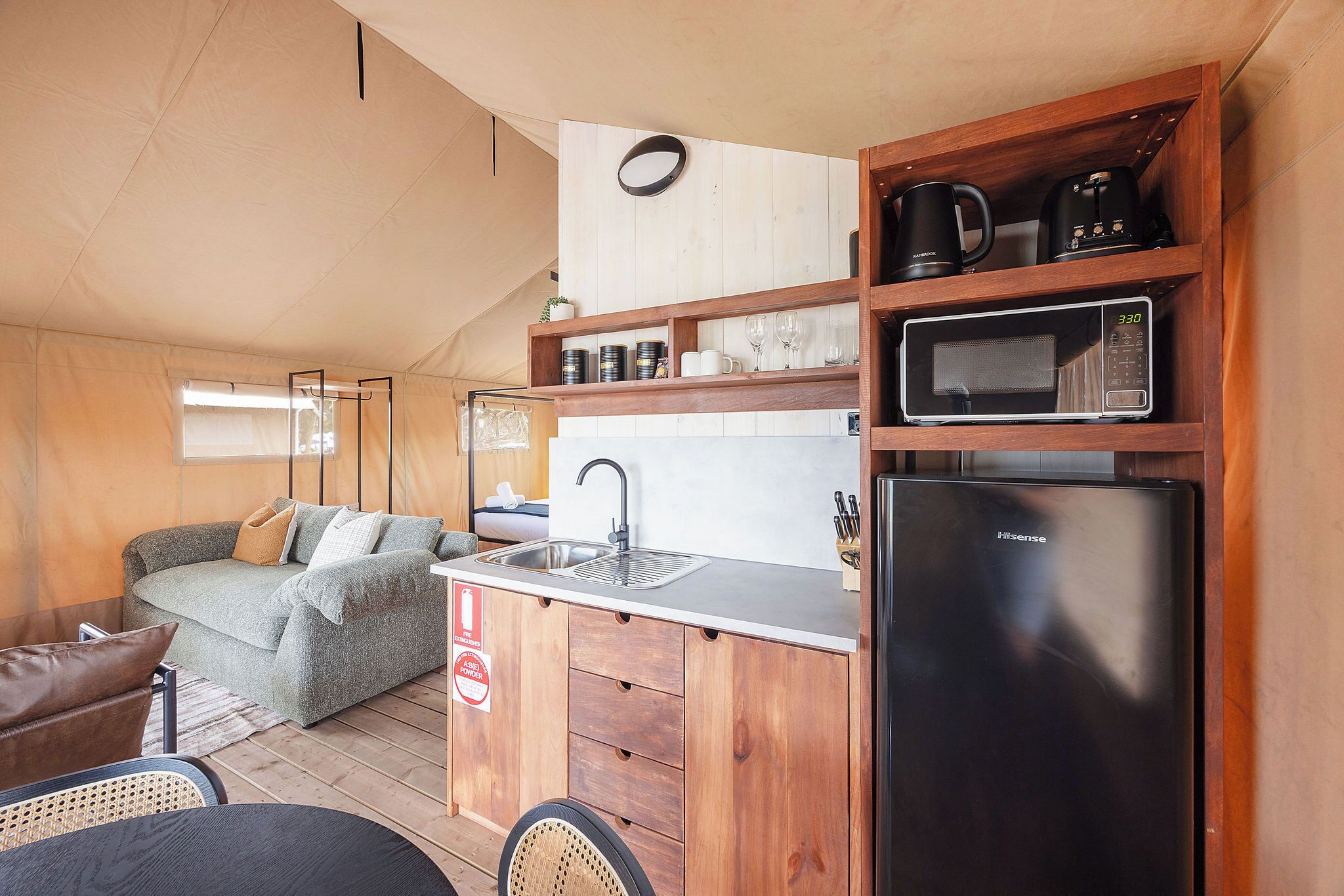 Cocina compacta con lavamanos, microondas y refrigerador, junto a un sofá y zona de comedor.