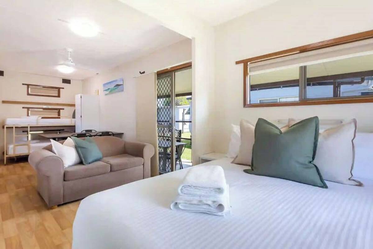 A hotel room with a bed, a sofa, a dining table, and a view of the outdoors.