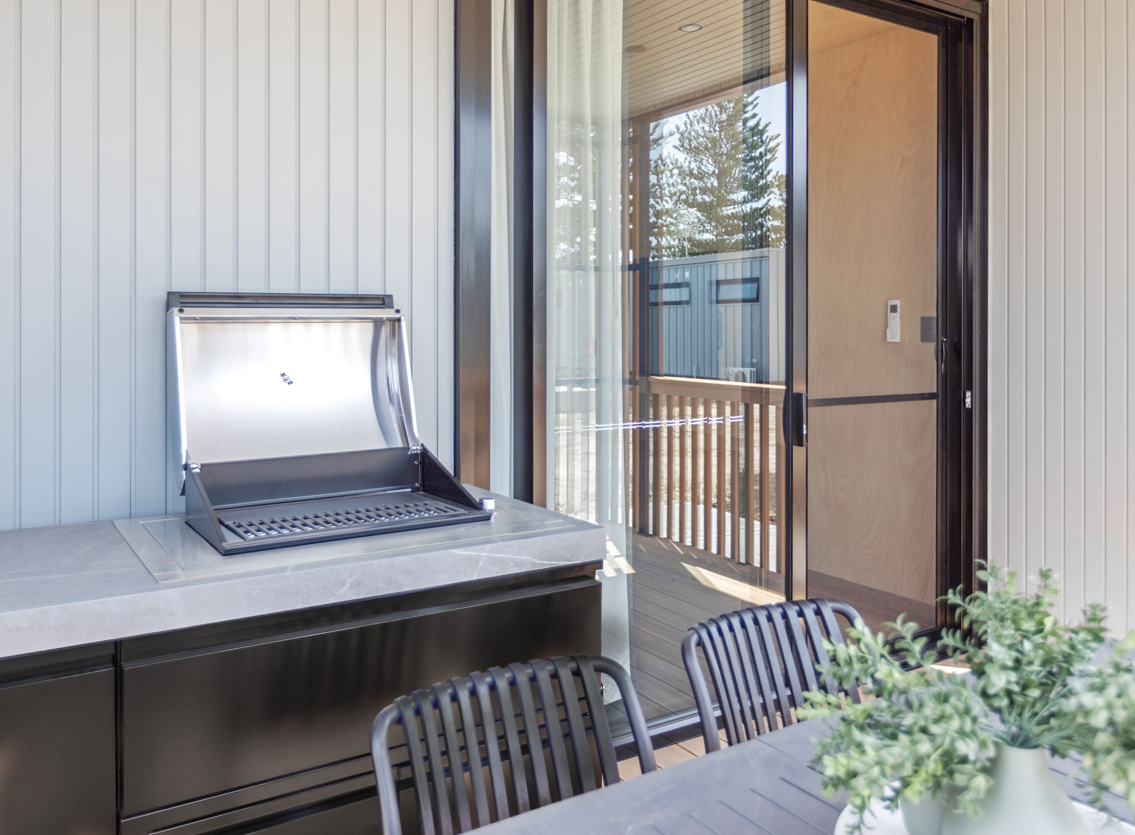 A balcony with a grill, a table, and chairs.