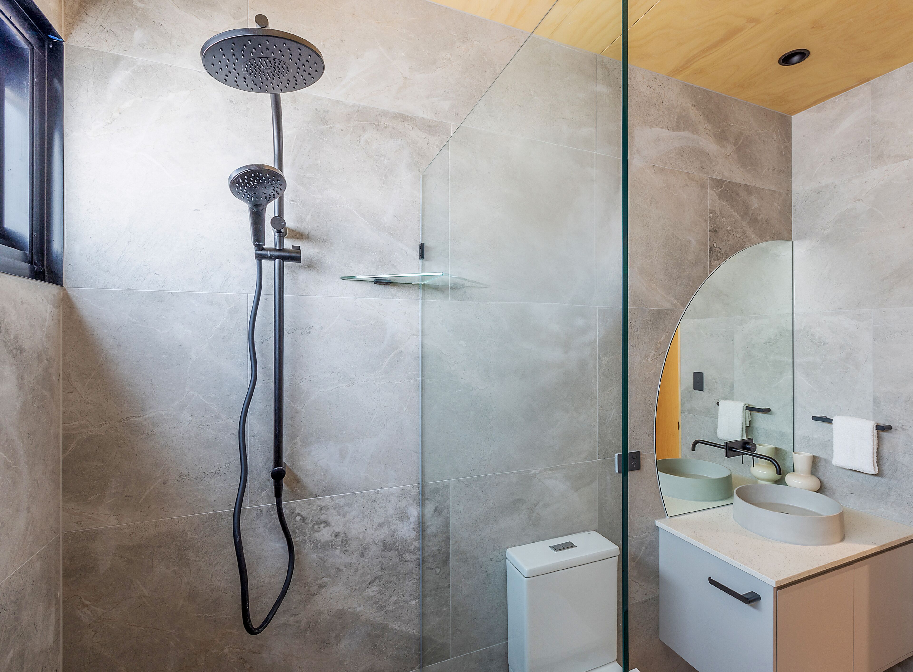 A modern bathroom with a glass-enclosed shower, a white toilet, and a vanity with a mirror and sink.