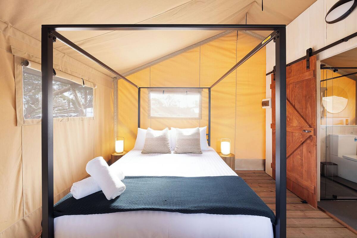 A tent-style room with a bed, a window, and a wooden door.