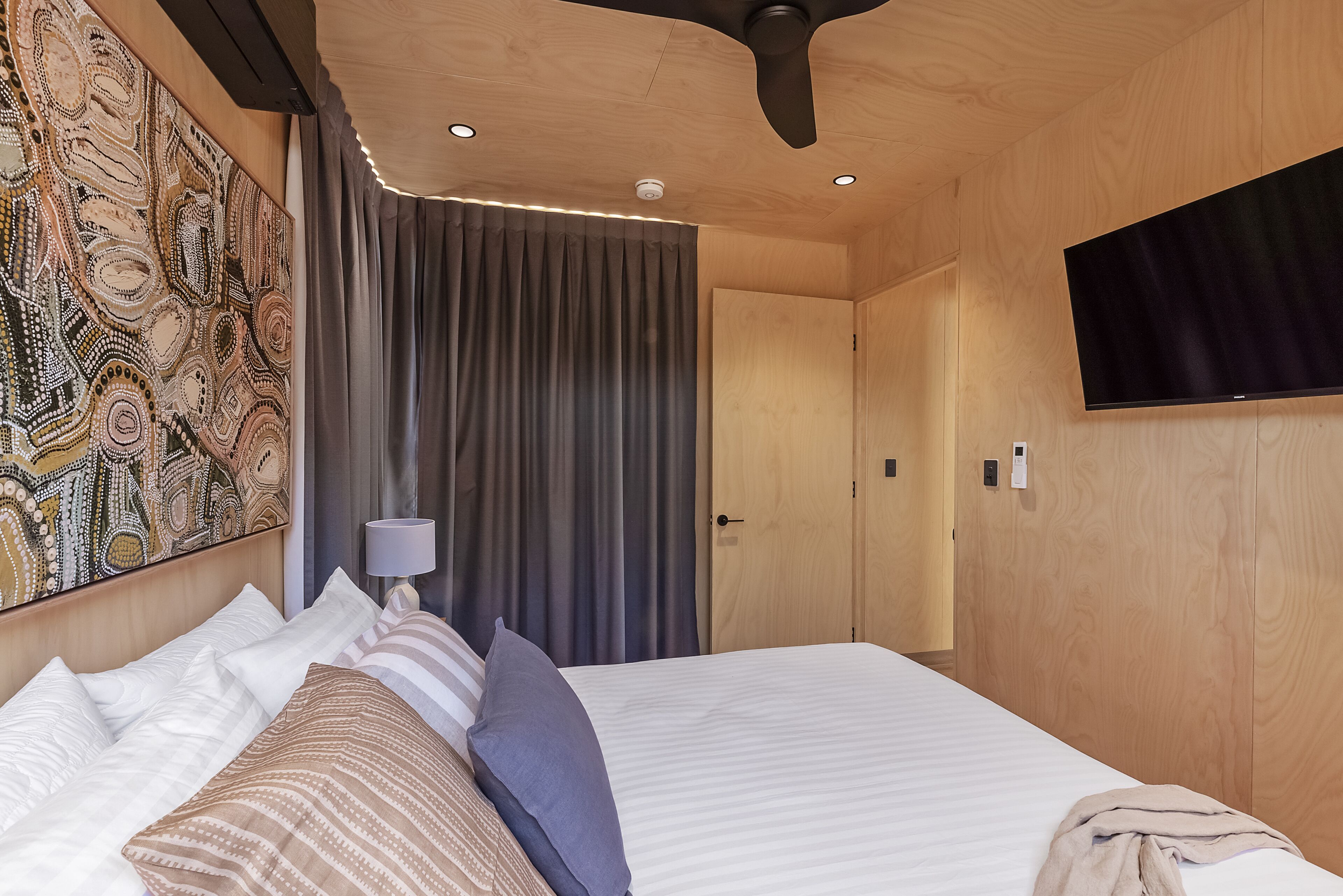 Een moderne hotelkamer met een groot bed, een plafondventilator, een flatscreen-tv en een decoratief wandobject.