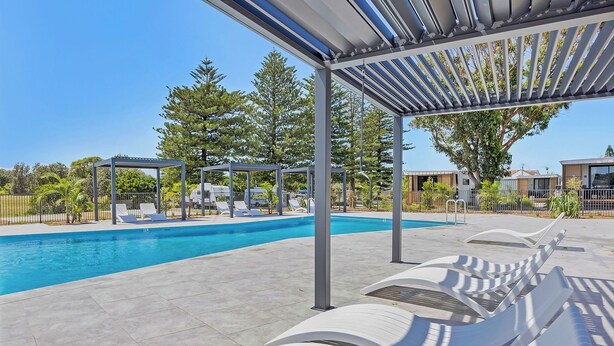 Una piscina con sillones de descanso y una pérgola.
