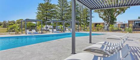 Una piscina con sillones de descanso y una pérgola.
