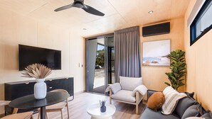 A modern living room with a flat-screen TV, a round coffee table, a sofa, and a dining area with chairs. - Reflections Hawks Nest - Holiday Park (Hawks Nest)