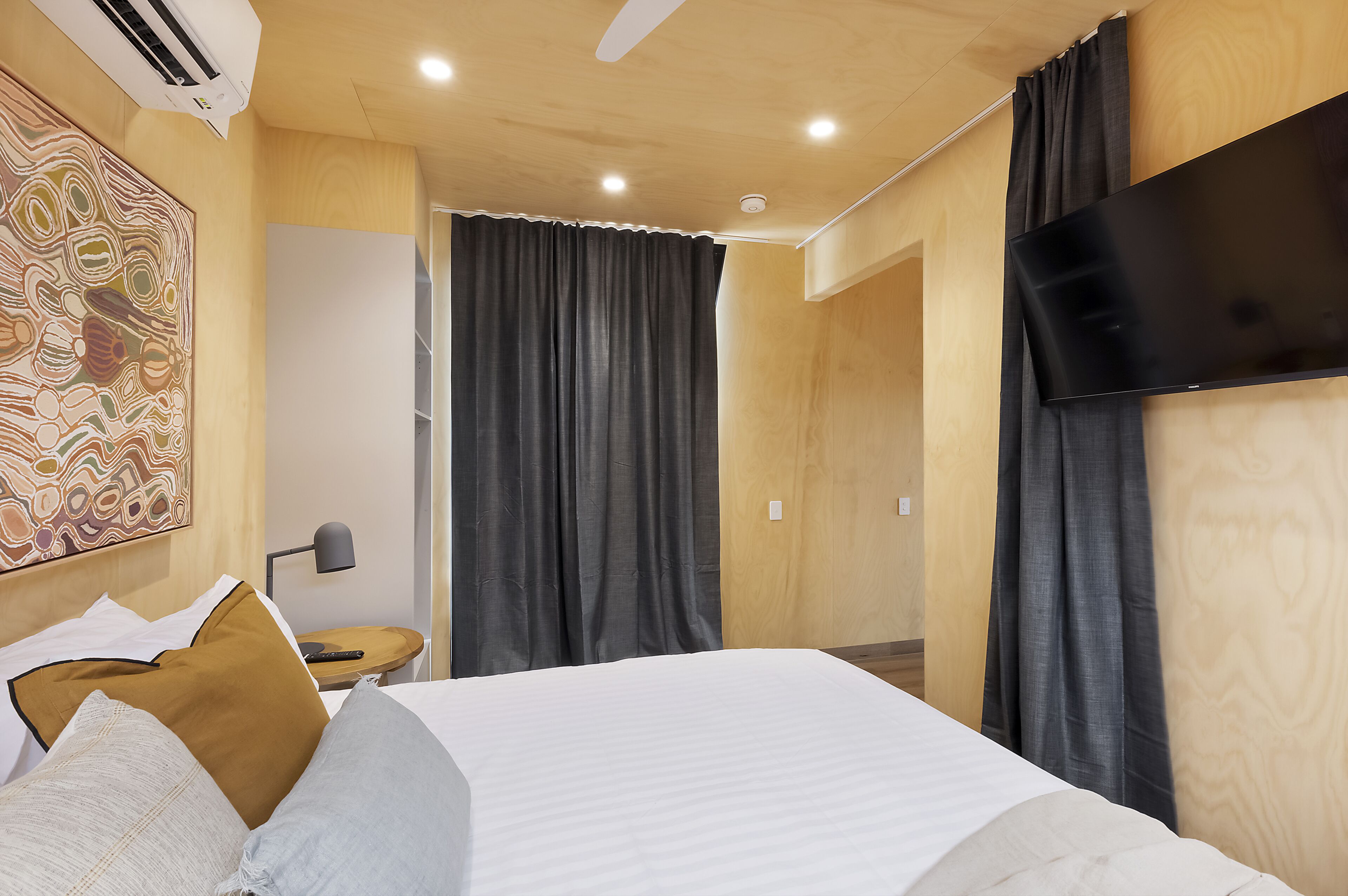Una habitación de hotel moderna con una cama grande, un televisor de pantalla plana en la pared y un ventilador de techo.