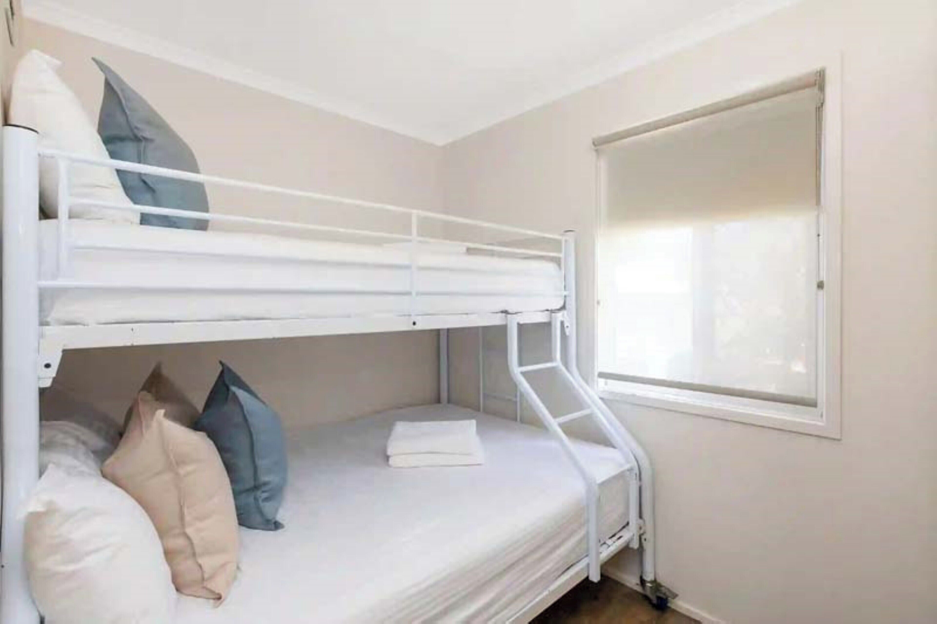 A bunk bed with a window, white walls, and a small window sill.