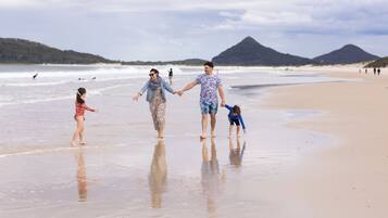 Una familia caminando por una playa con montañas al fondo.