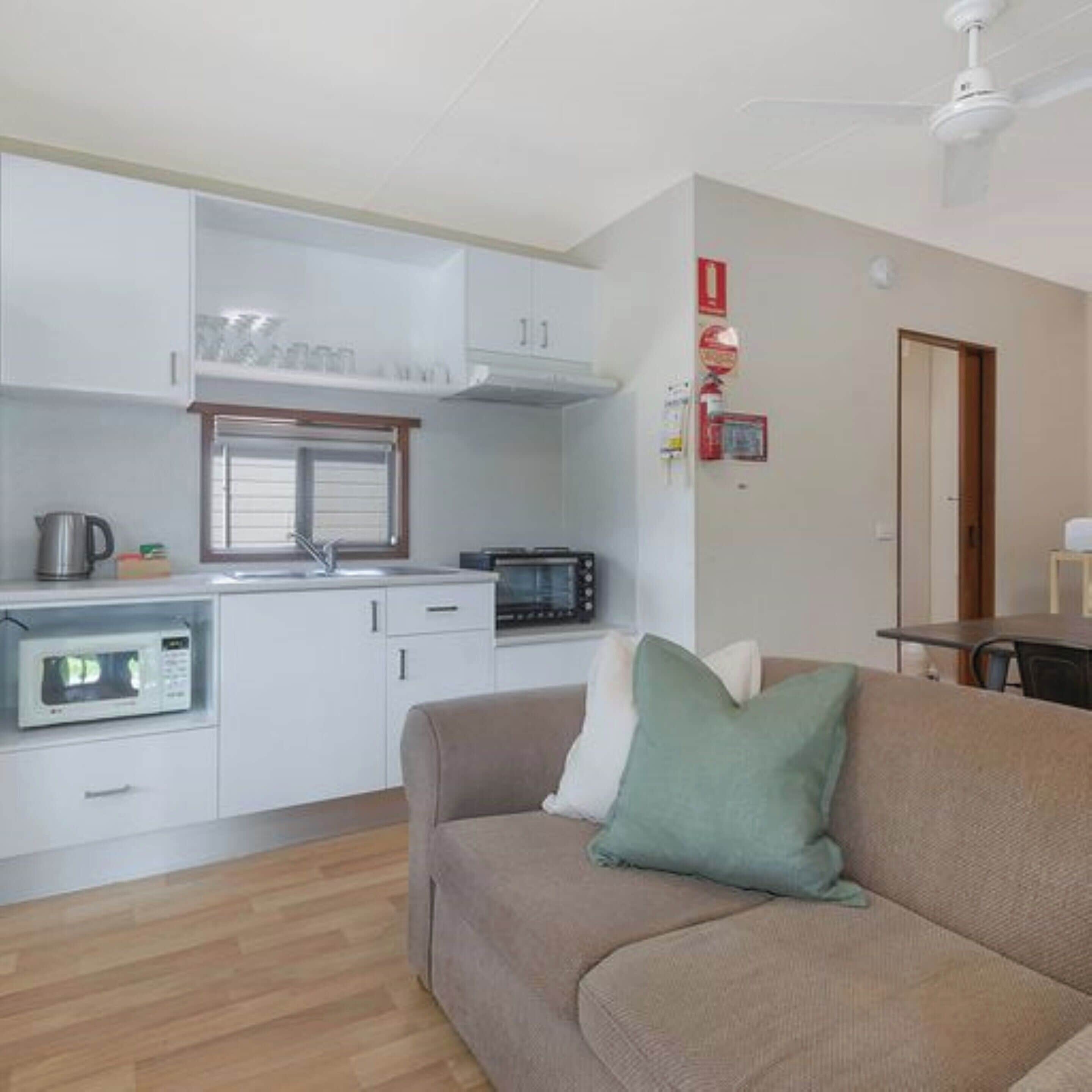 Un espacio habitable compacto con kitchenette, un sofá con cojines y un ventilador de techo.
