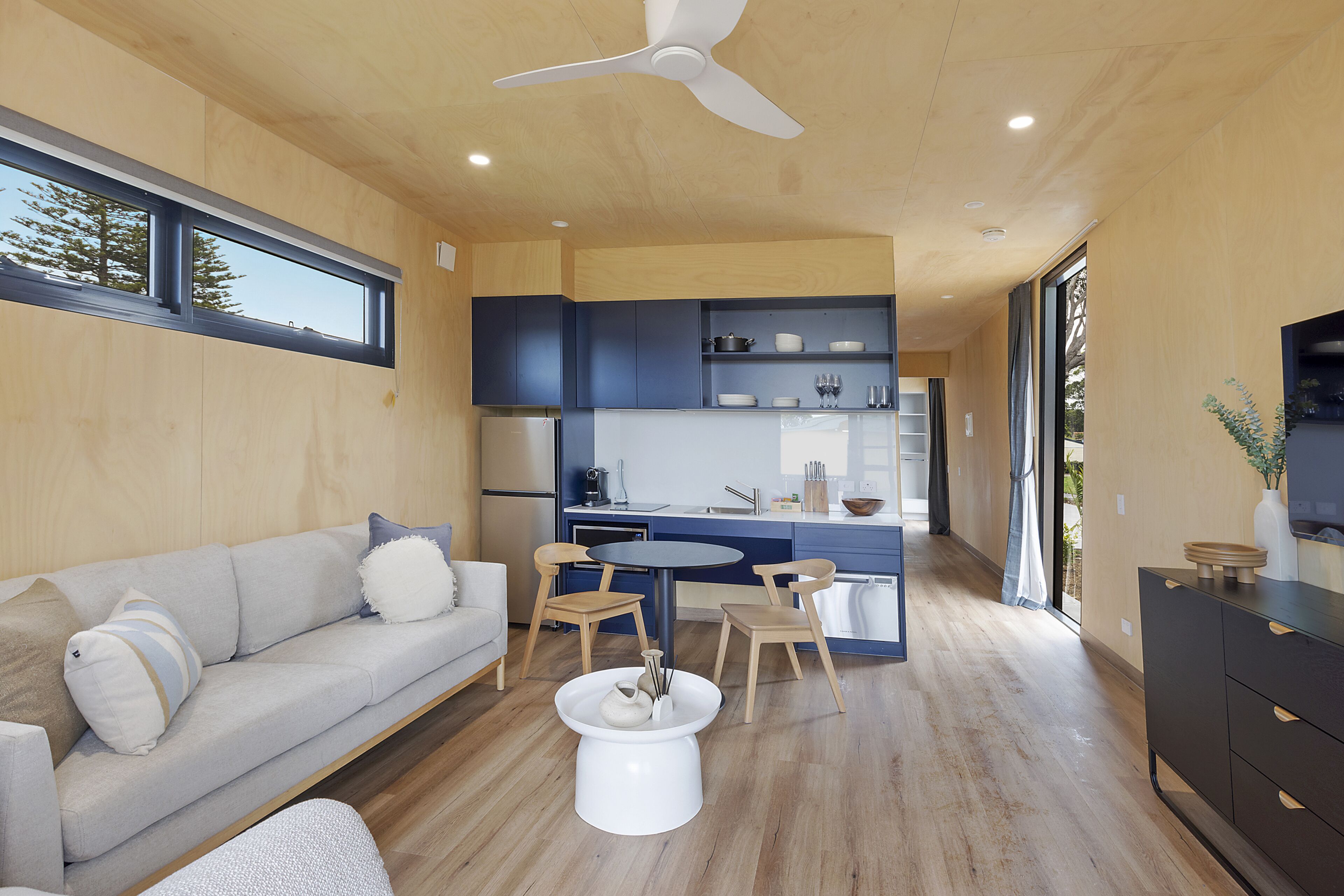 Una cocina moderna con electrodomésticos integrados, un comedor con una mesa redonda y sillas, y una sala de estar con sofá y mesa de centro.