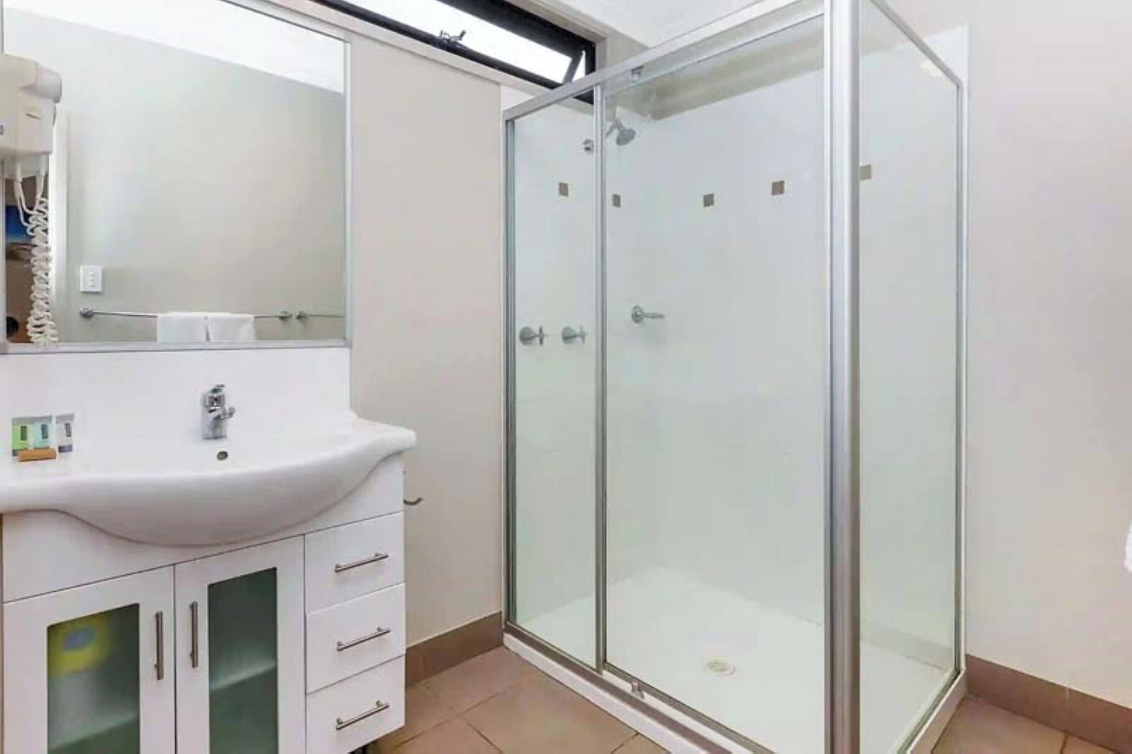 Ein modernes Badezimmer mit einer Duschkabine aus Glas, einem weißen Waschbecken und einem Spiegel darüber.
