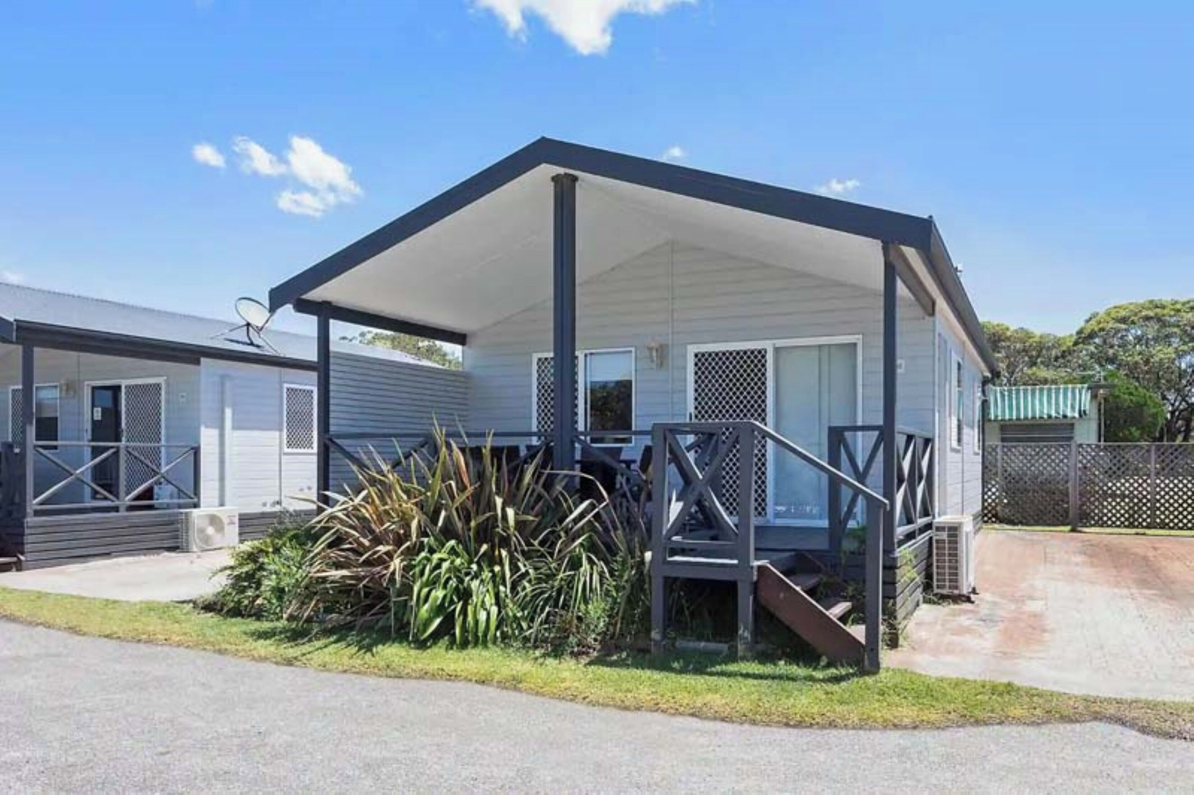 A single-story mobile home with a covered porch, a satellite dish, and a small garden area.