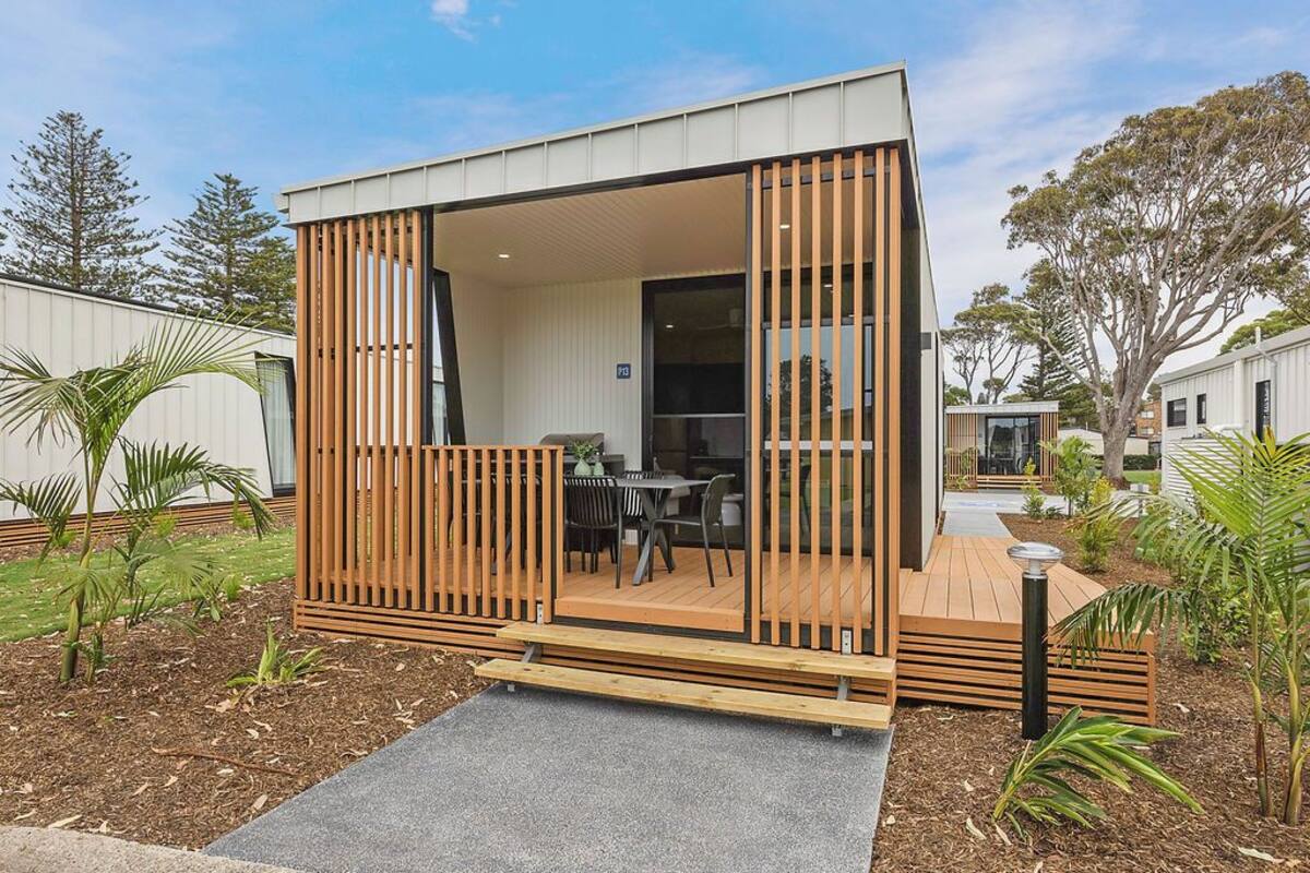 A modern, compact mobile home with a wooden deck, a dining area, and a large sliding glass door.