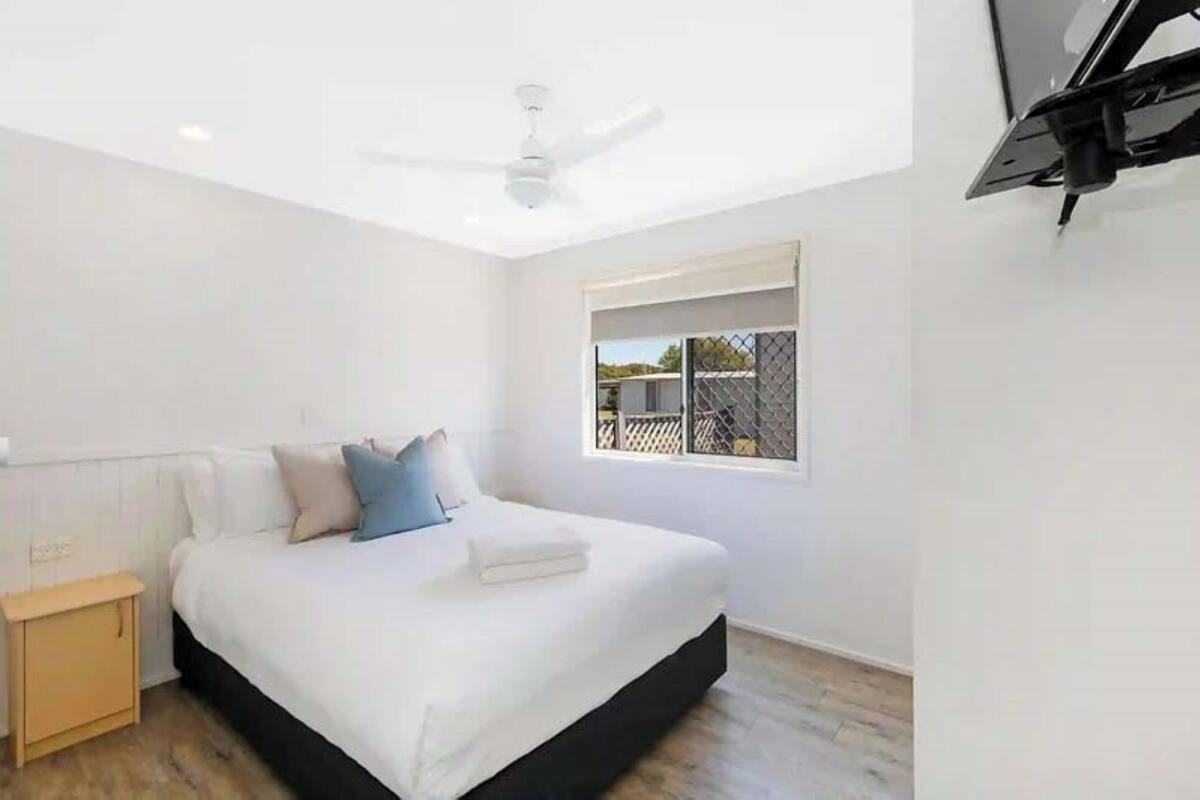 A modern bedroom with a large bed, a ceiling fan, a window with a view, and a small bedside table.