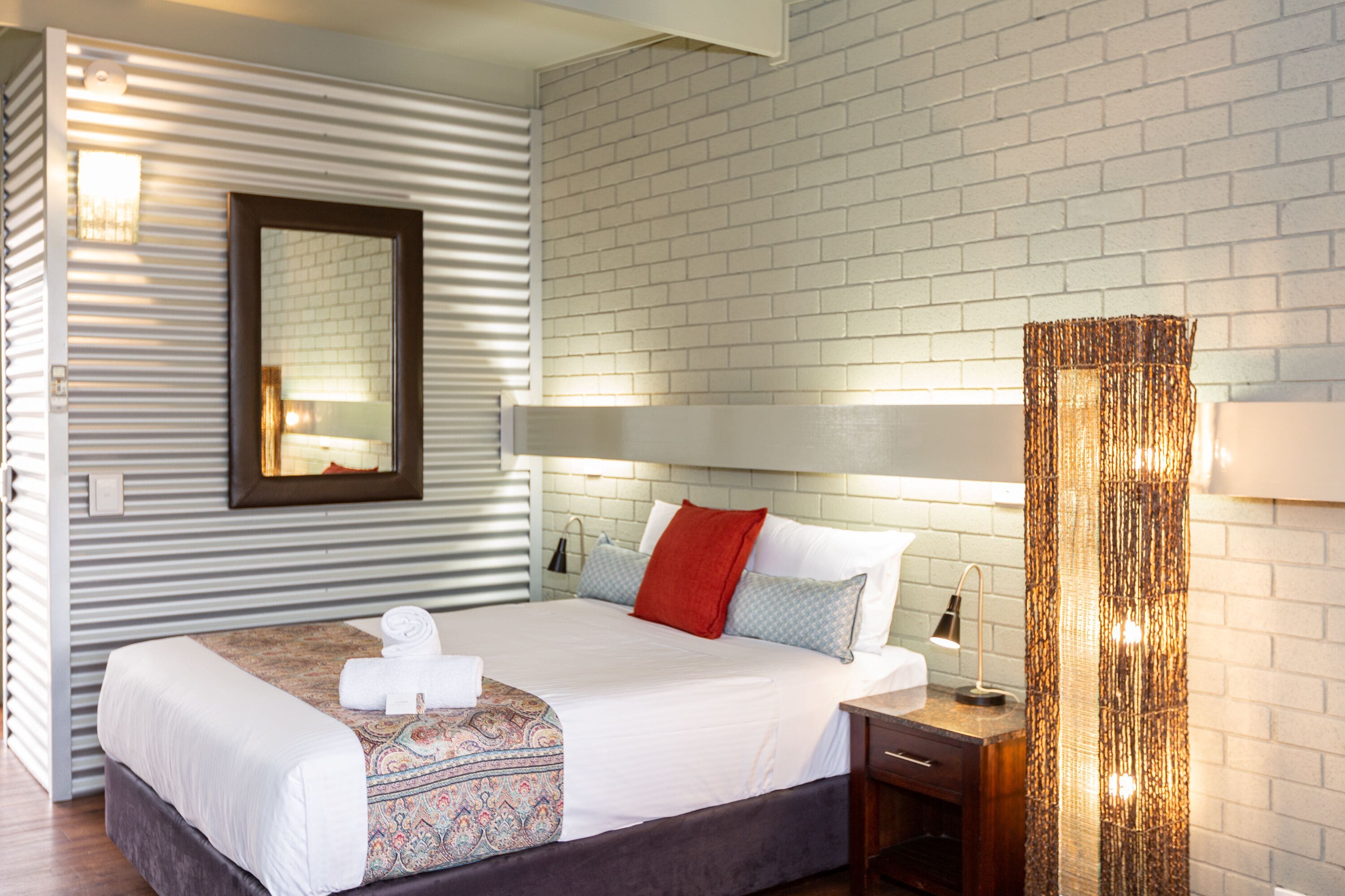 Une chambre d’hôtel avec un grand lit, une table de chevet, un miroir et un mur au motif de briques.