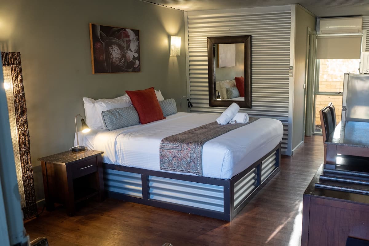 Habitación de hotel moderna con una cama grande, mesitas de noche, un espejo y un escritorio con una silla.