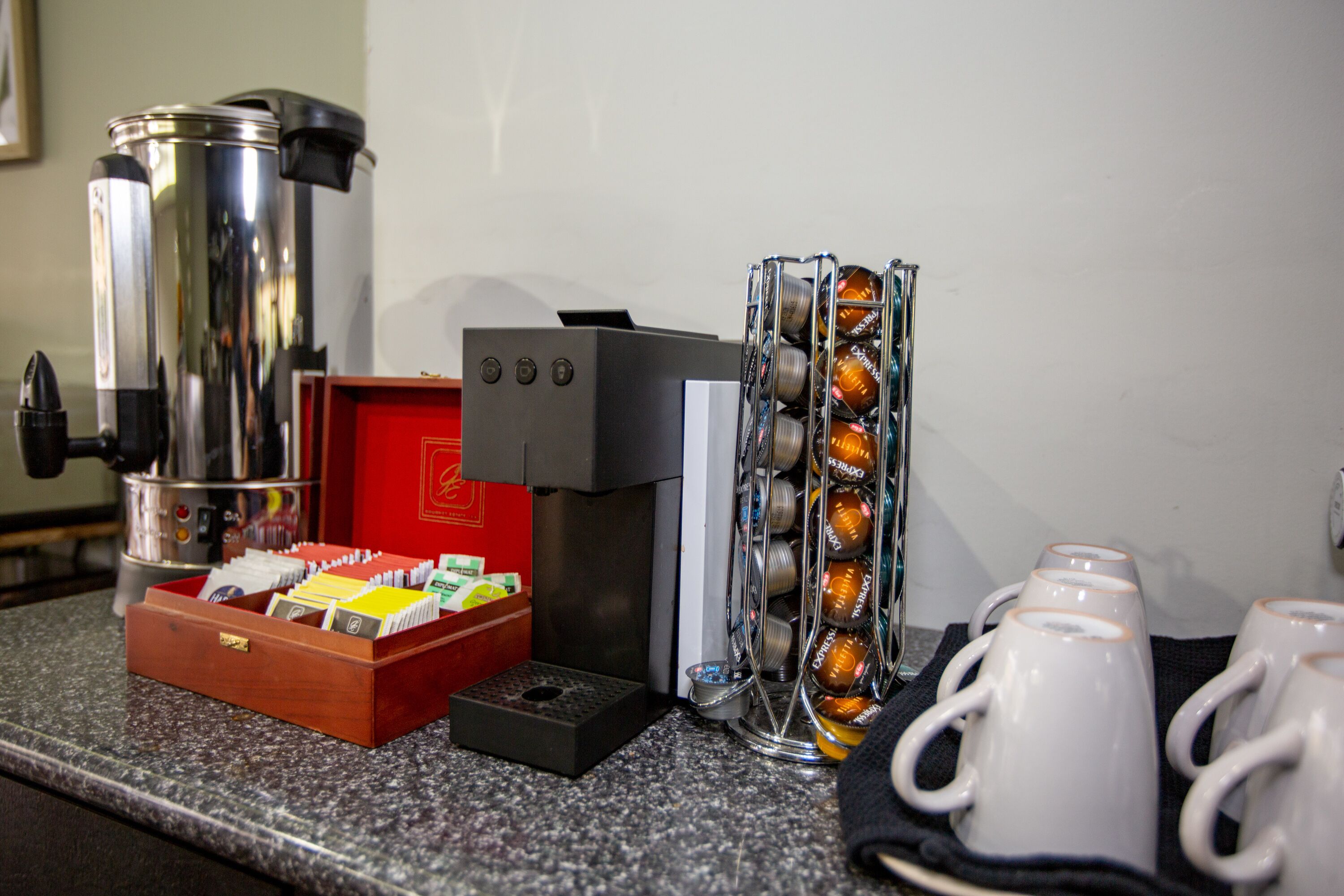A coffee station with a coffee maker, a coffee grinder, a box of coffee pods, and a mug rack.