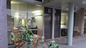 Un edificio con fachada de vidrio, números en las puertas y mesas al aire libre.