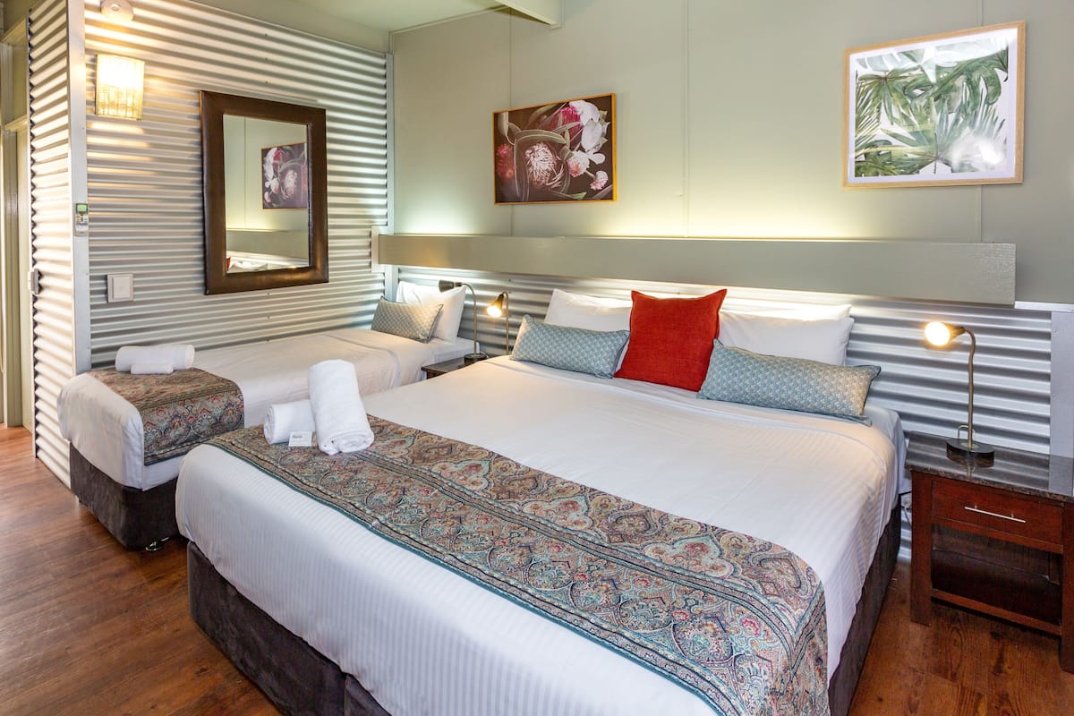 Una habitación de hotel con una cama grande, dos camas más pequeñas, un espejo y obras de arte en las paredes.