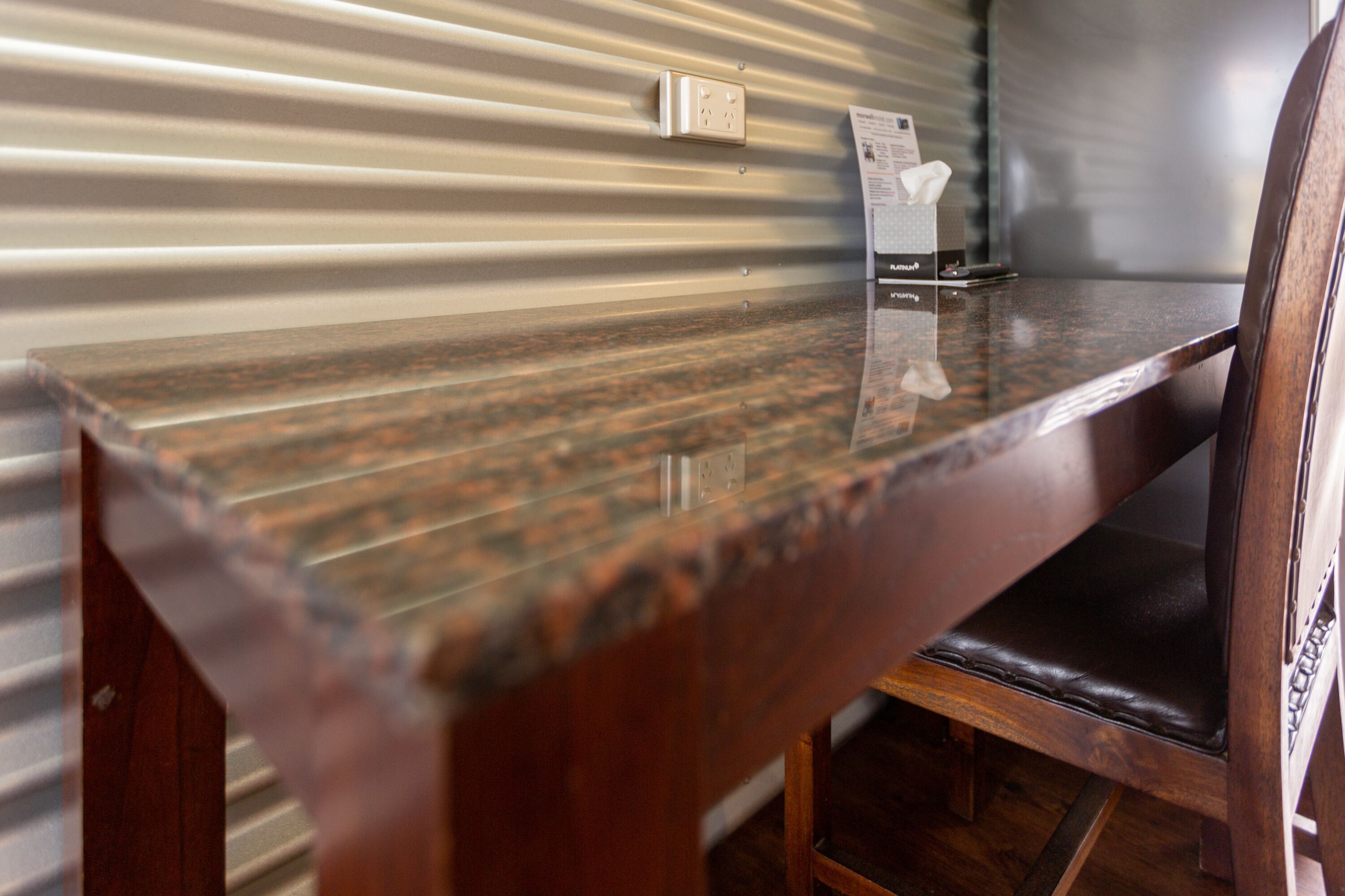 A wooden table with a reflective surface, a chair with a cushioned seat, and a wall with a corrugated metal design.