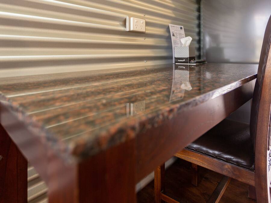 A wooden table with a reflective surface, a chair with a cushioned seat, and a wall with a corrugated metal design.