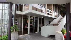 Entrada de un edificio con mostrador de recepción, puertas de vidrio y una escalera que sube a un nivel superior.