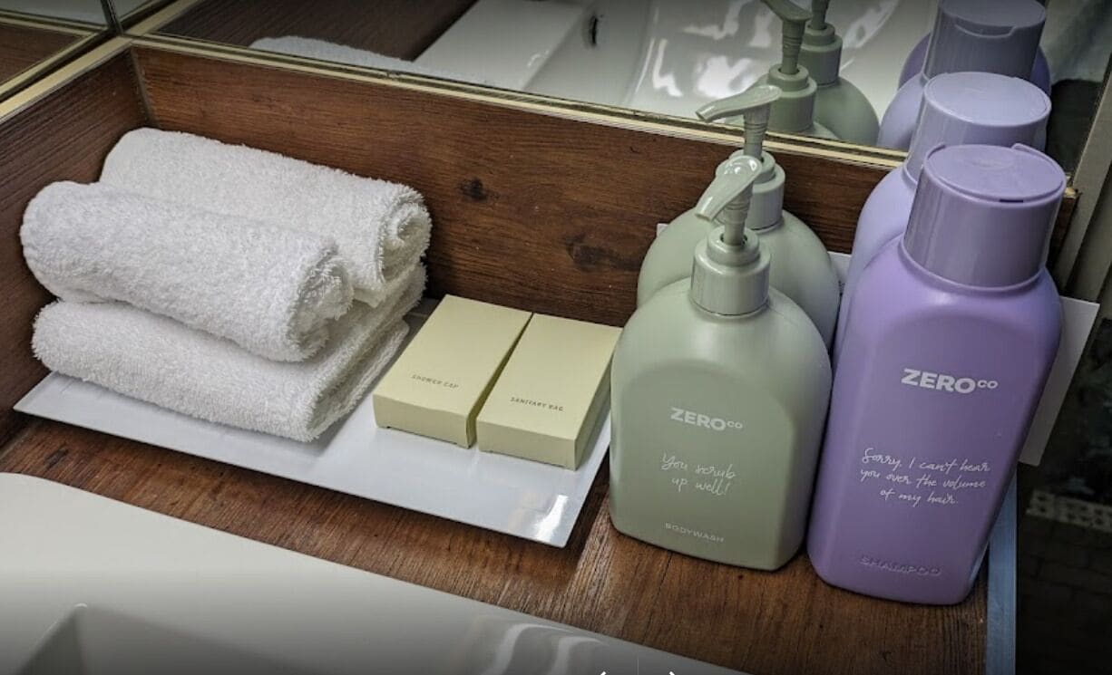 Et badeværelsesbord med spejl, et håndklæde, en sæbe, bodywash og en shampoo-flaske.
