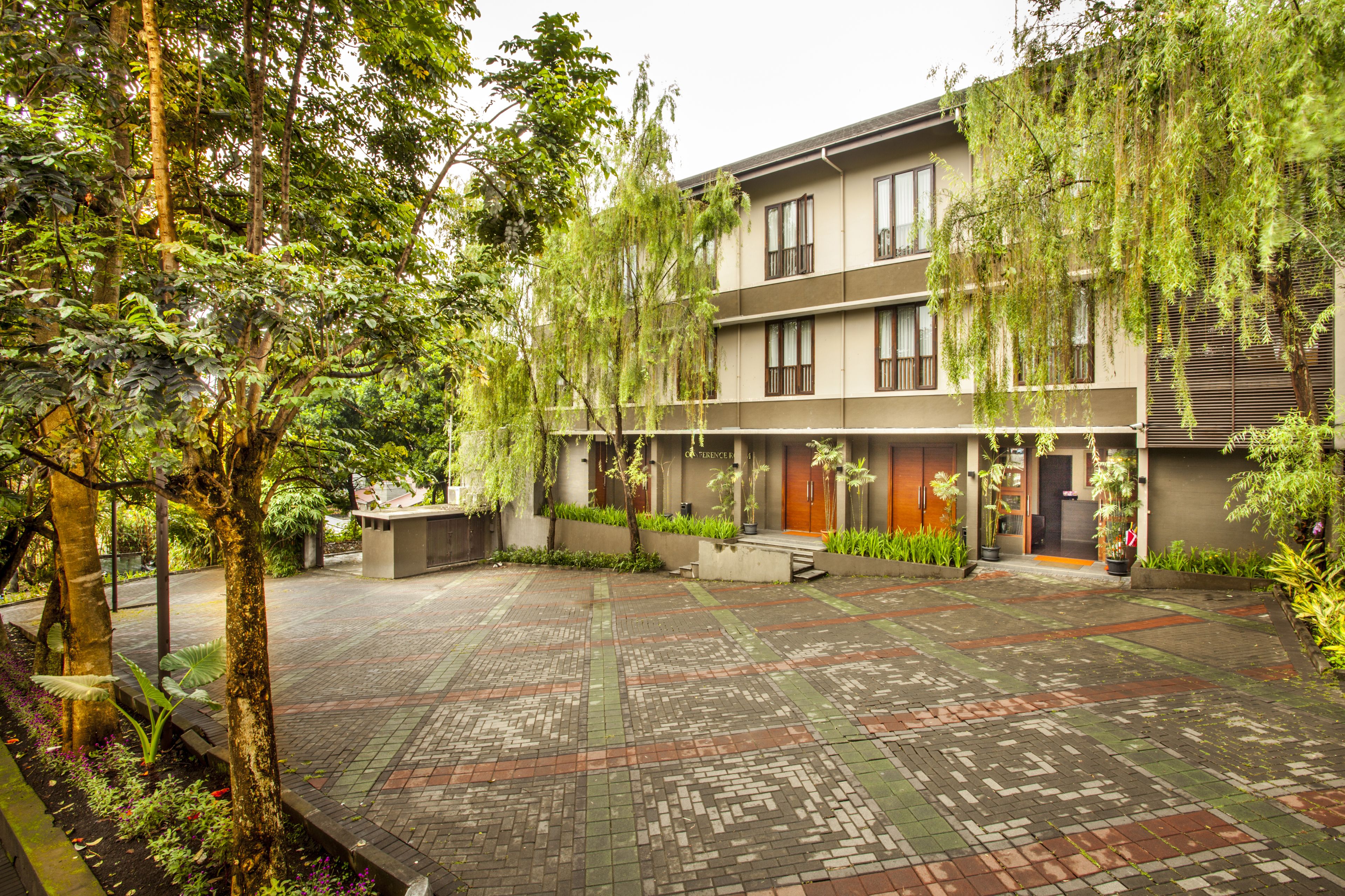 A courtyard with a brick pathway, a building with multiple balconies, and lush greenery.
