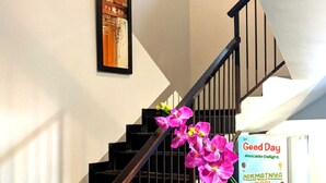 Una escalera con barandilla negra y paredes blancas, un cuadro enmarcado en la pared, y un letrero que dice 'Good Day' y 'Avocado Delight'.