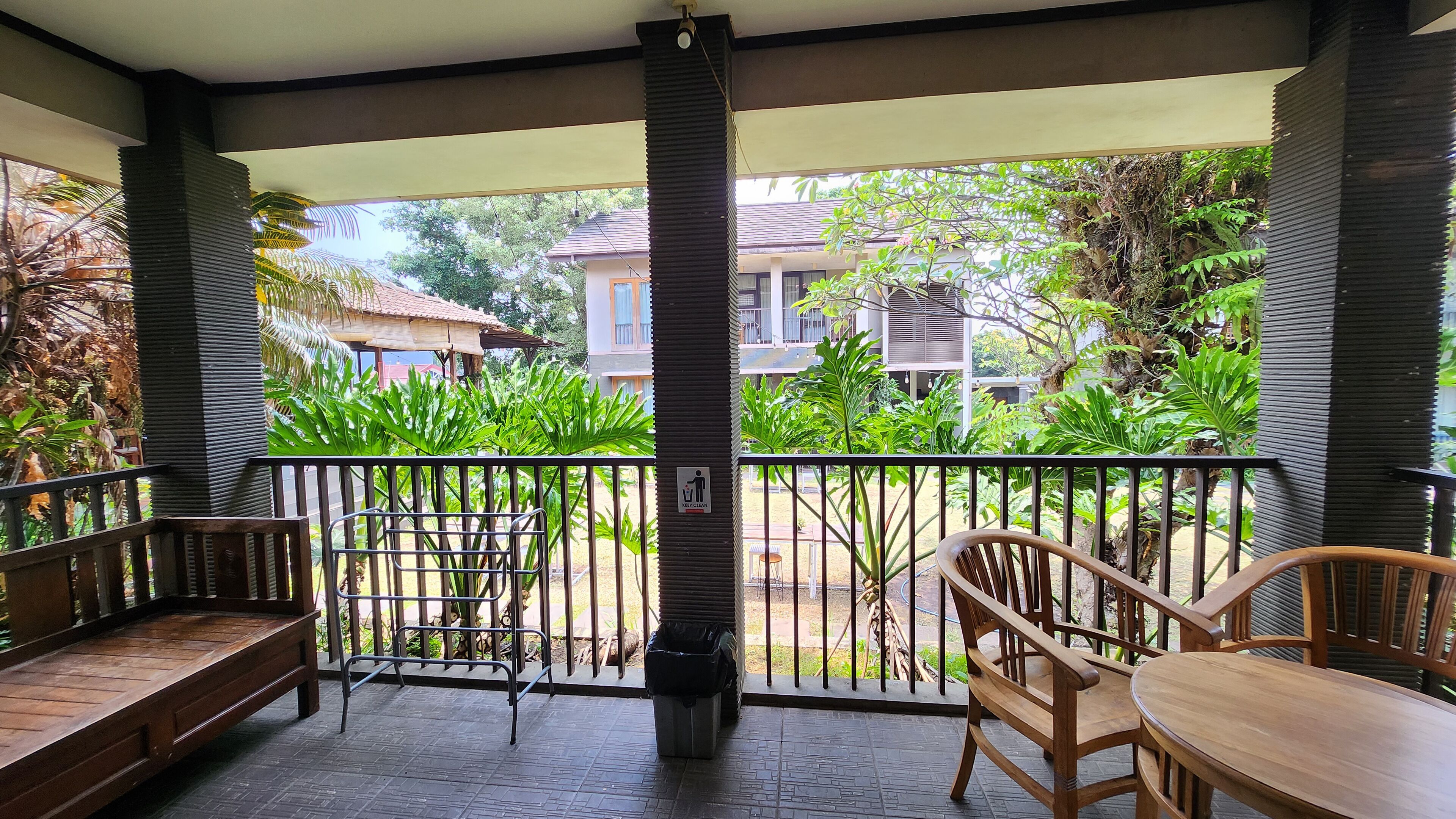 Een overdekt balkon met een metalen hekwerk, een houten bank en een tafel met stoelen.