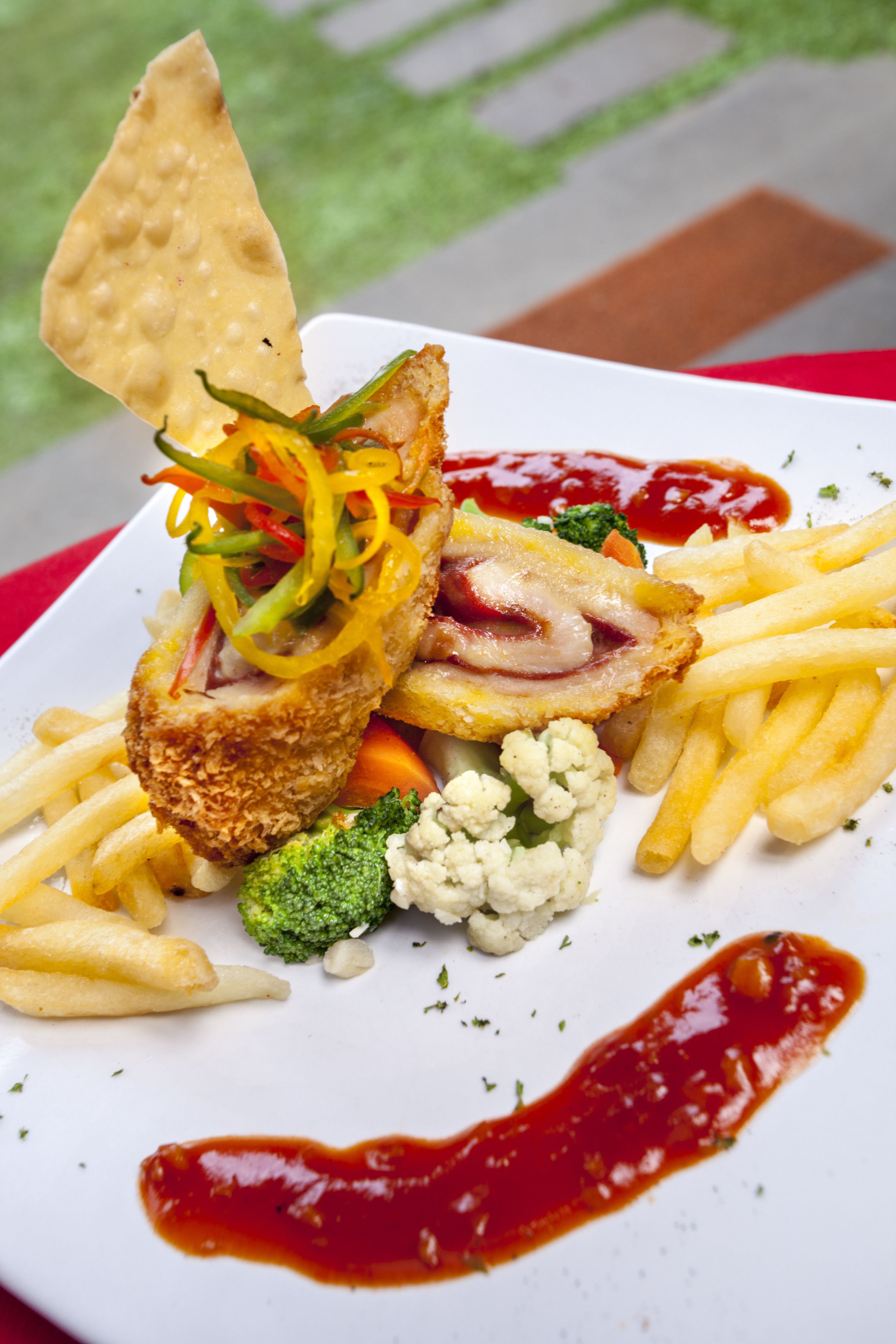 A plate of food with a breaded cutlet, fries, broccoli, cauliflower, and a cracker.
