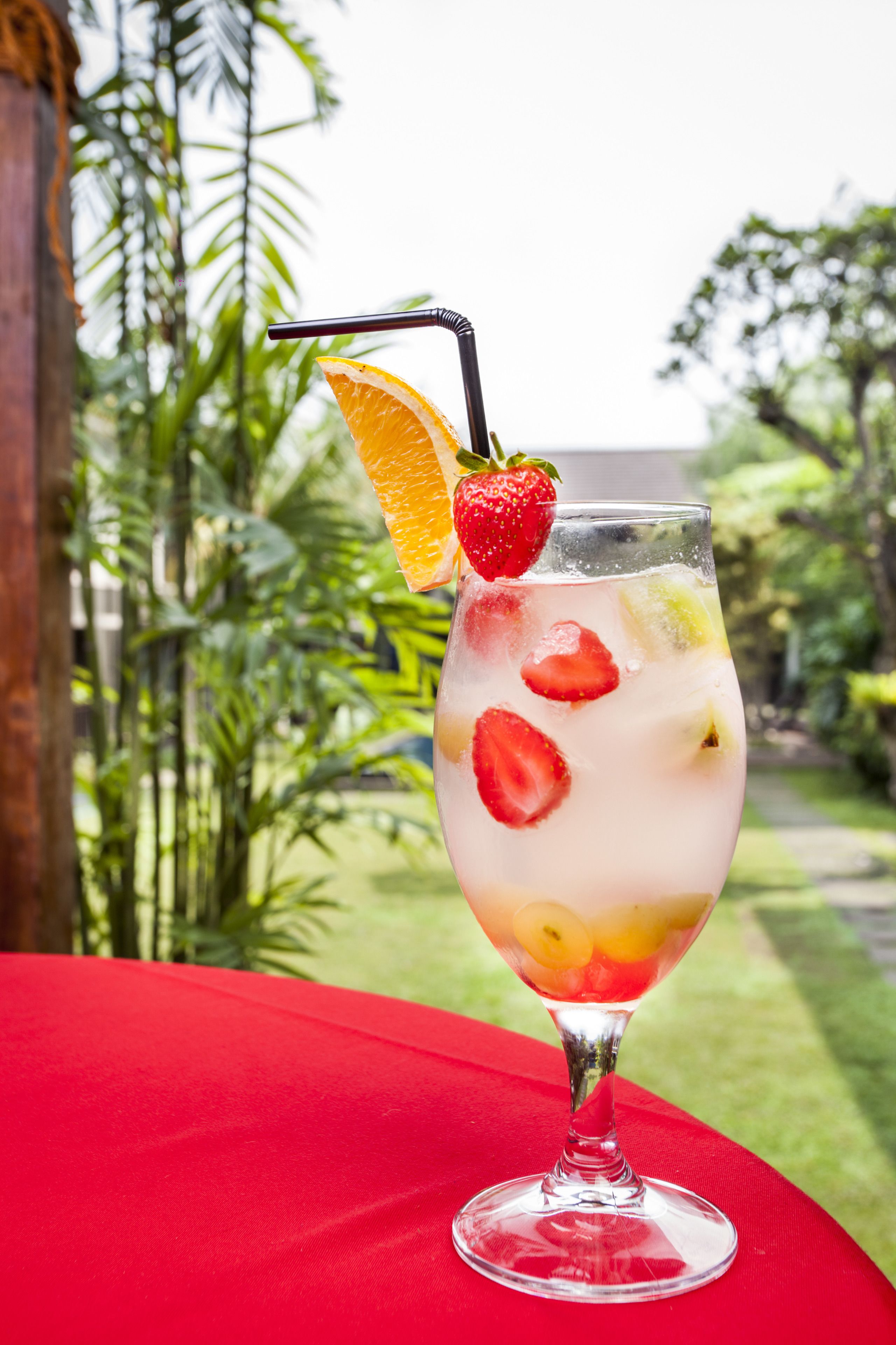 A cocktail glass with fruit slices and a straw on a red table.