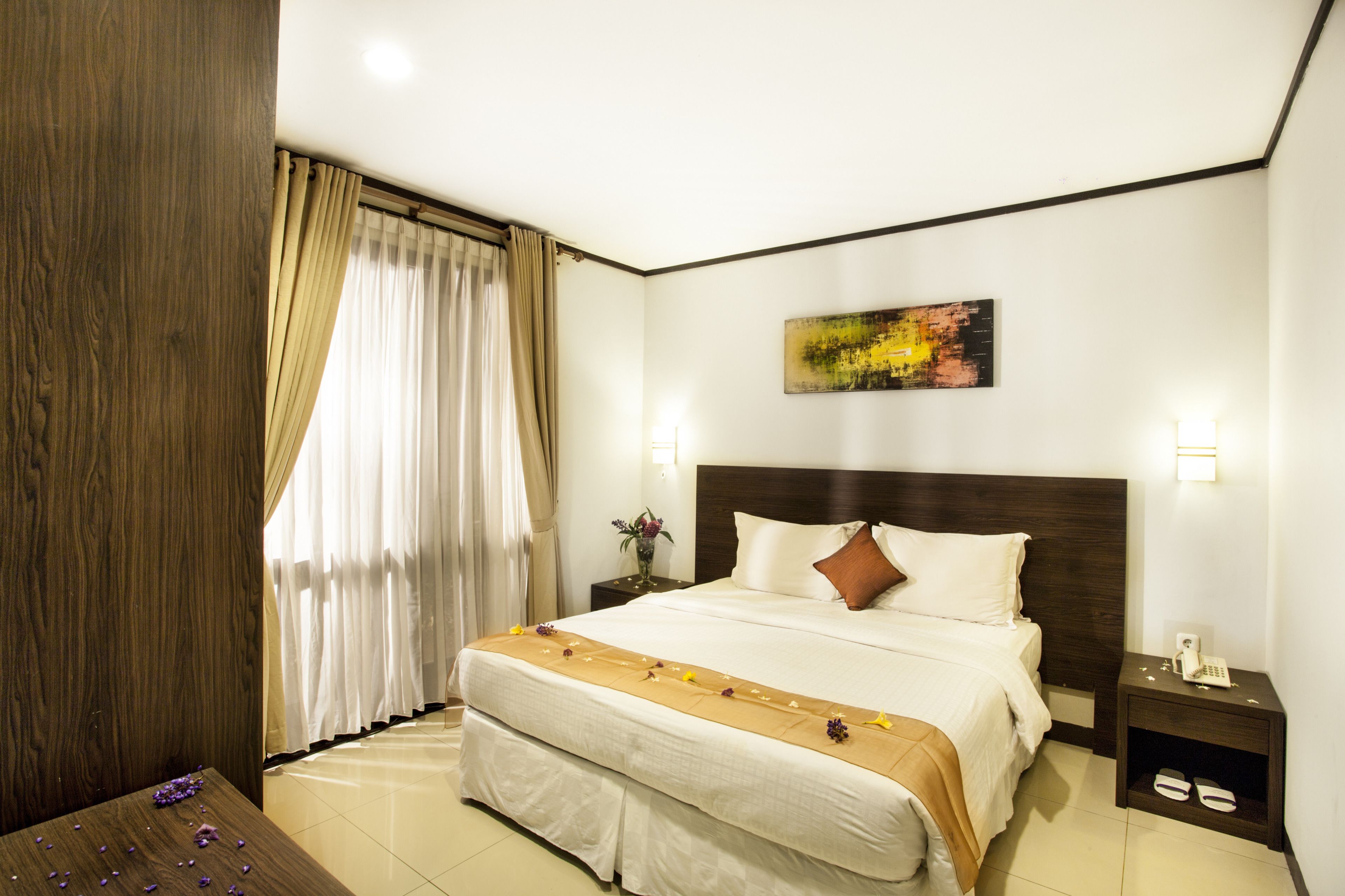 Una camera d'albergo con un letto grande, una testiera in legno, un comodino con un telefono e un quadro appeso al muro.