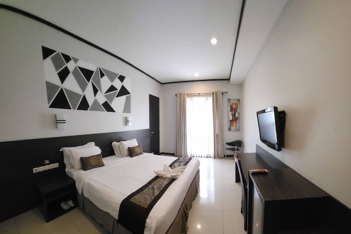 A modern hotel room with a large bed, a flat-screen TV, a desk, and a decorative wall piece.