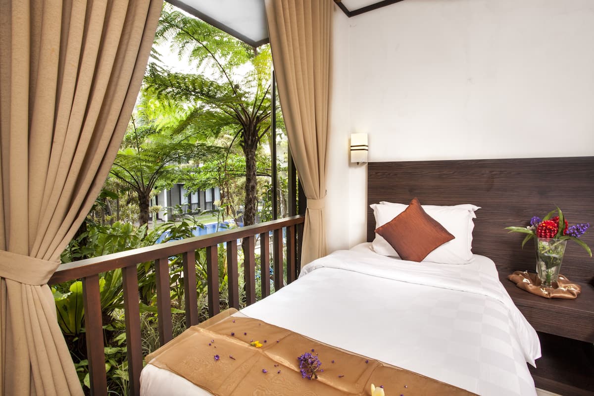 A bedroom with a bed, curtains, a nightstand, and a view of greenery outside.
