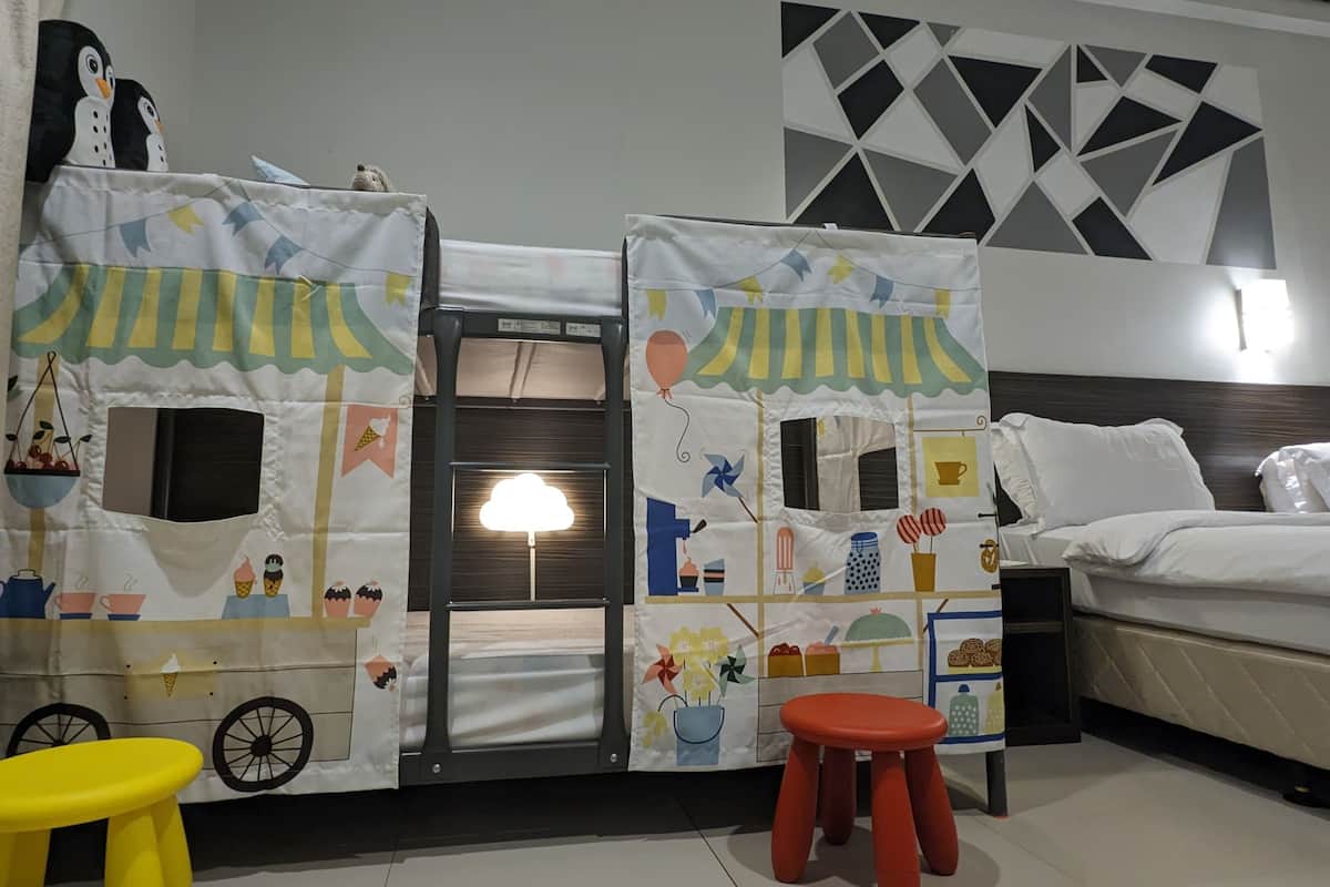 A hotel room with a bed, a small stool, a table, and a curtain with a playful design.