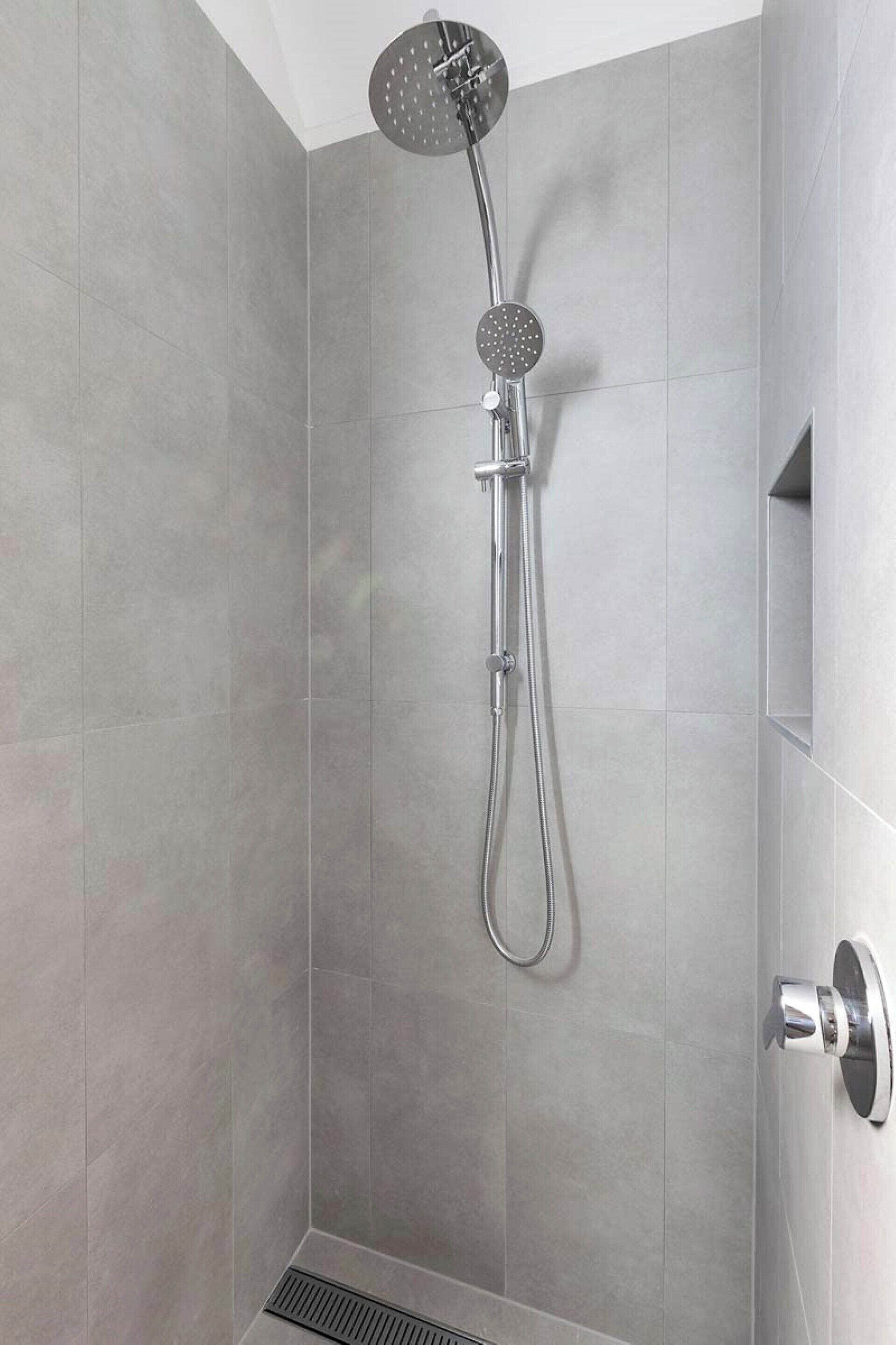 Eine Dusche mit Handbrause und am Wand montiertem Wasserhahn in einem gefliesten Raum.
