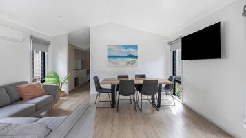 A modern living room with a grey sofa, a dining table with six chairs, and a large window.
