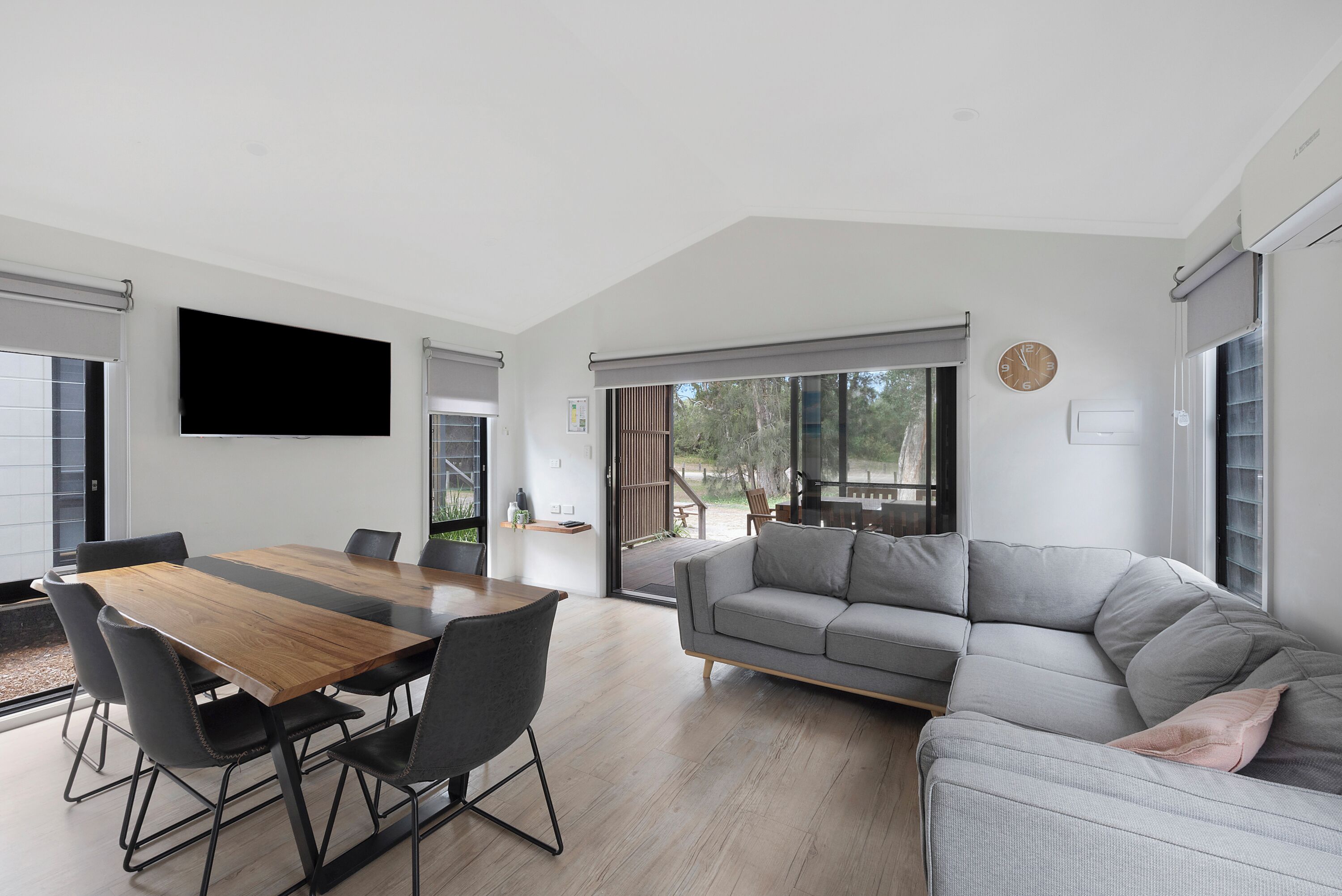 Una sala moderna con una mesa de comedor de madera, un sofá gris y sillas negras.
