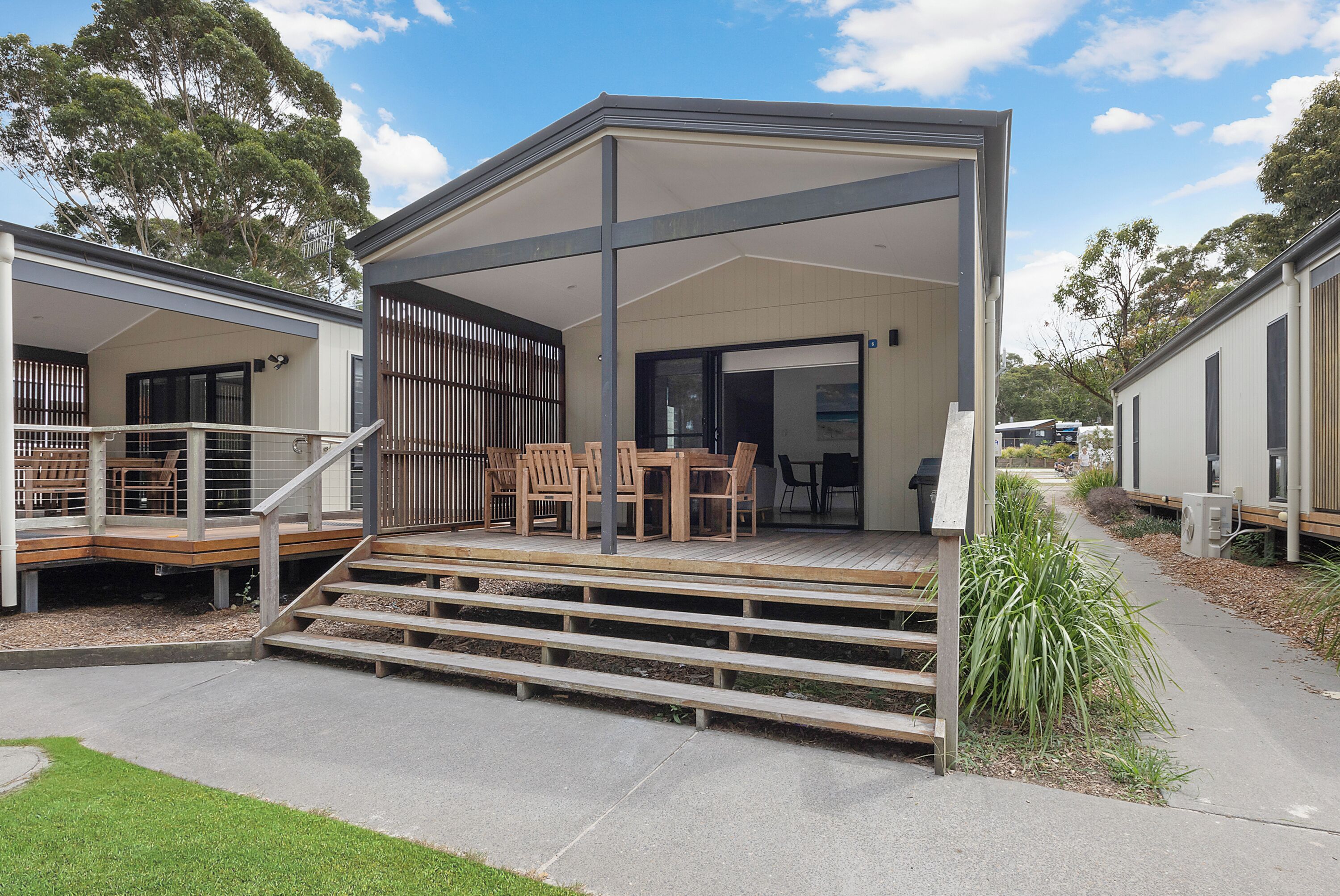 A modern building with a covered outdoor area, wooden steps, and outdoor furniture.