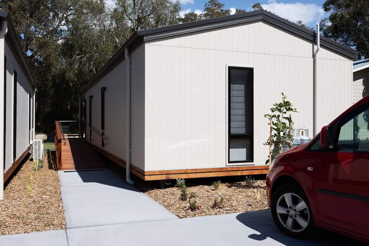 A modern mobile home with a wooden deck and a car parked in front.