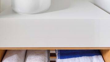 Un baño moderno con un espejo redondo, un lavabo blanco y una repisa de madera encima.