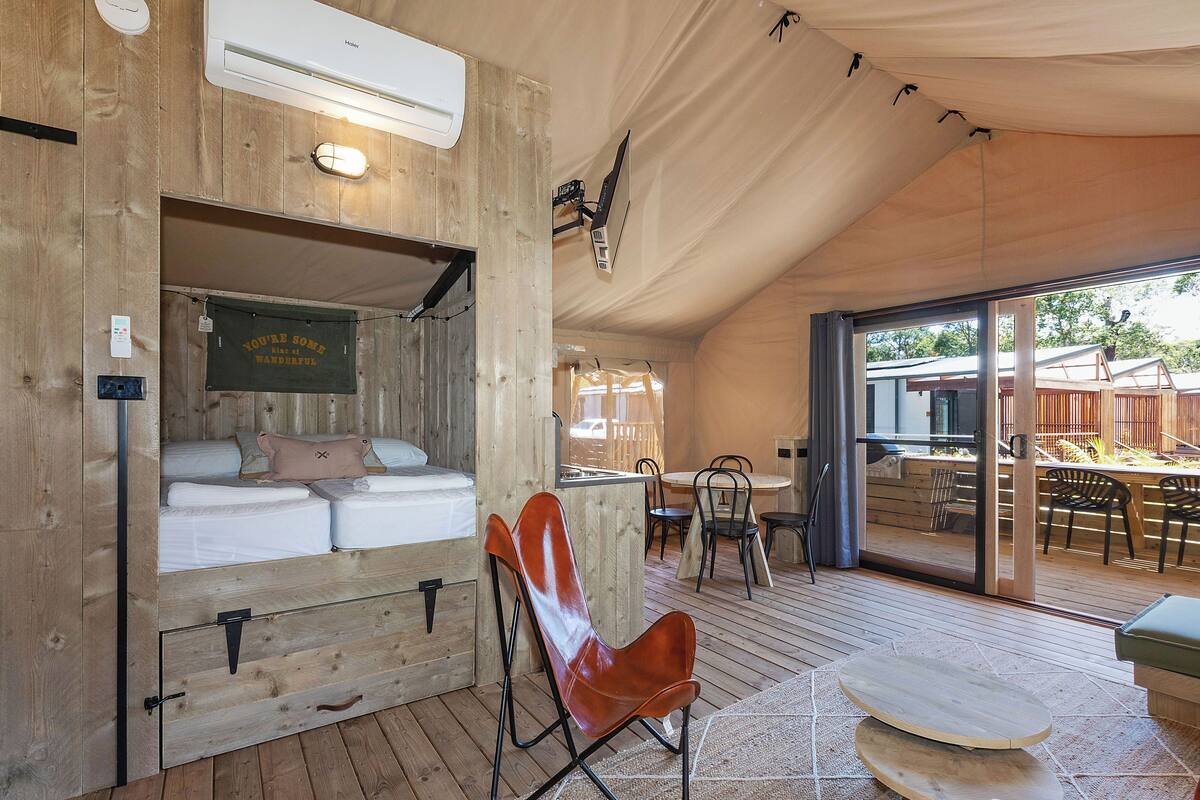 A wooden interior with a bed, a dining area, and a large sliding glass door to an outdoor patio.