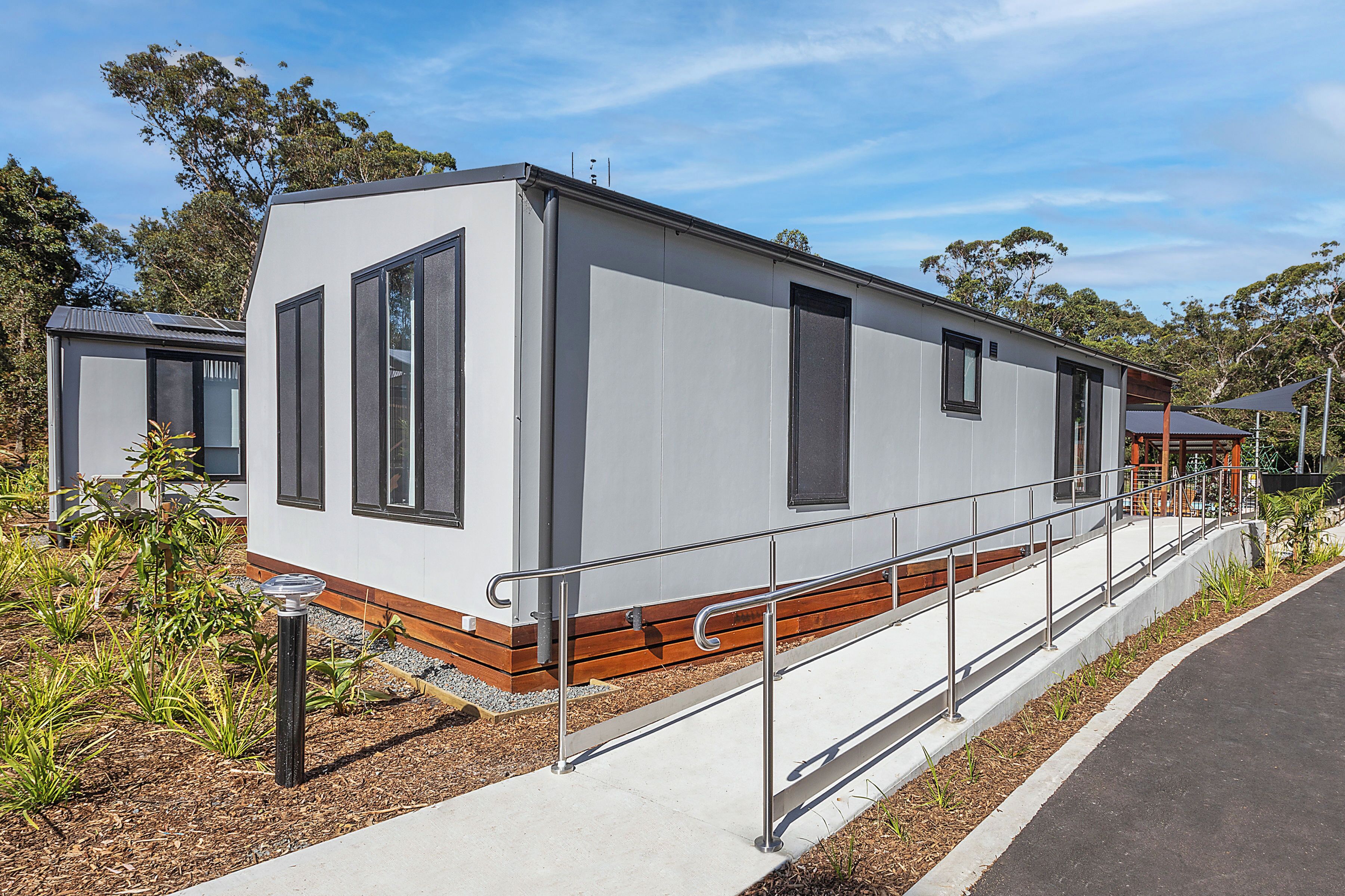 A modern, single-story mobile home with a flat roof, large windows, and a small porch area.